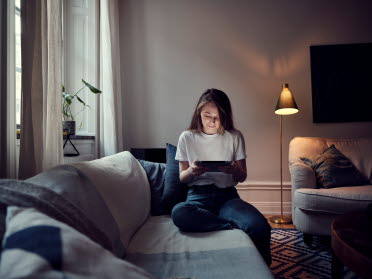 Kvinna som sitter i sitt vardagsrum på sin soffa och läser på sin tablet